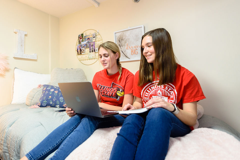Two students sit on a bed, working on homework.
