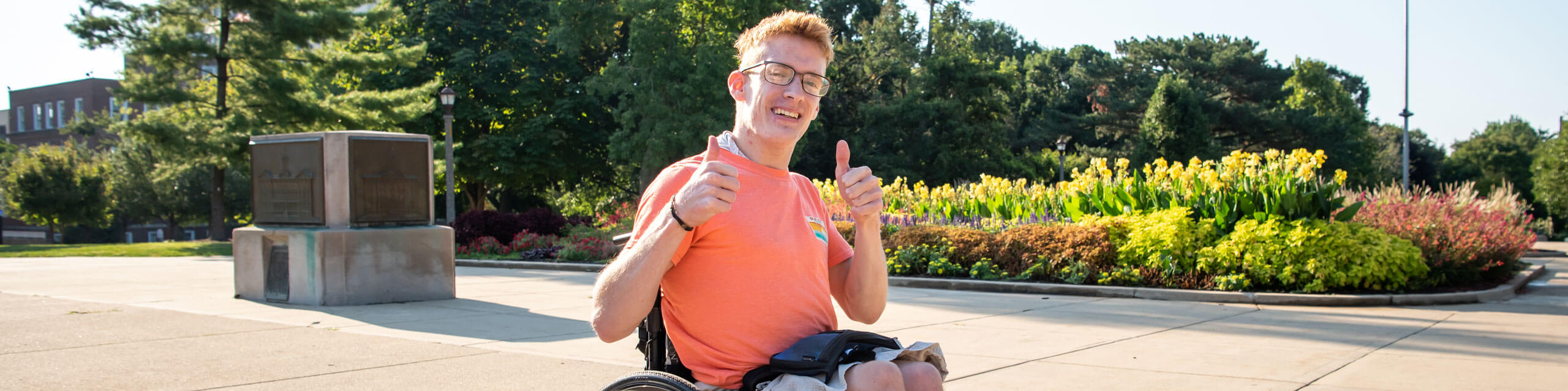 A student in a wheelchair gives two thumbs-up to the camera.
