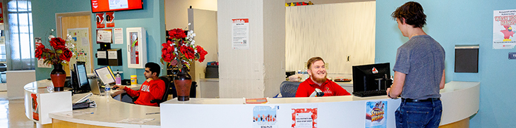 Reception desk with two employees and a visitor in a brightly lit office.